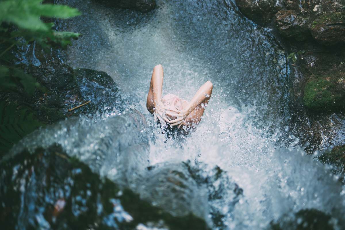 pool high-angle photography of woman bathing below waterfalls during daytime woman