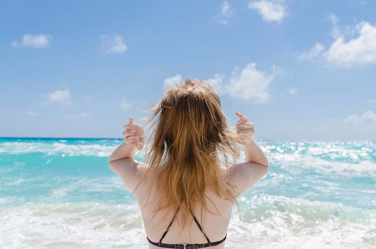 beach woman wearing black bra raising both arms facing towards the sea at daytime sea