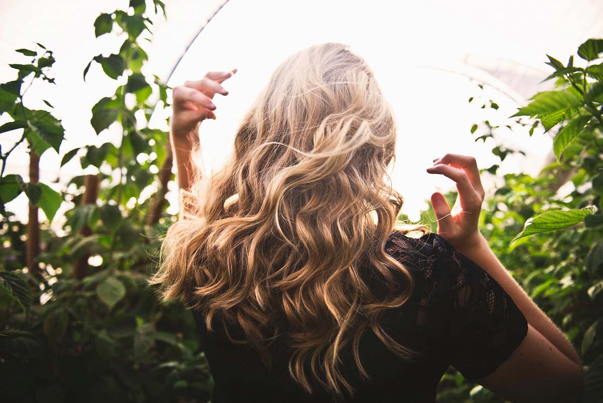 hair blonde haired woman in black top surrounded by tall plants blonde