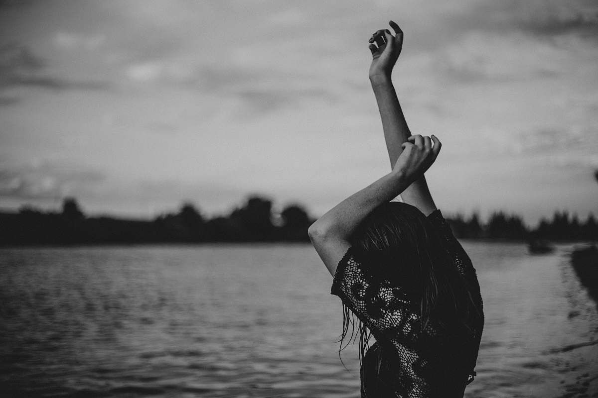 black-and-white grayscale photo of woman stretching body front of body of water water