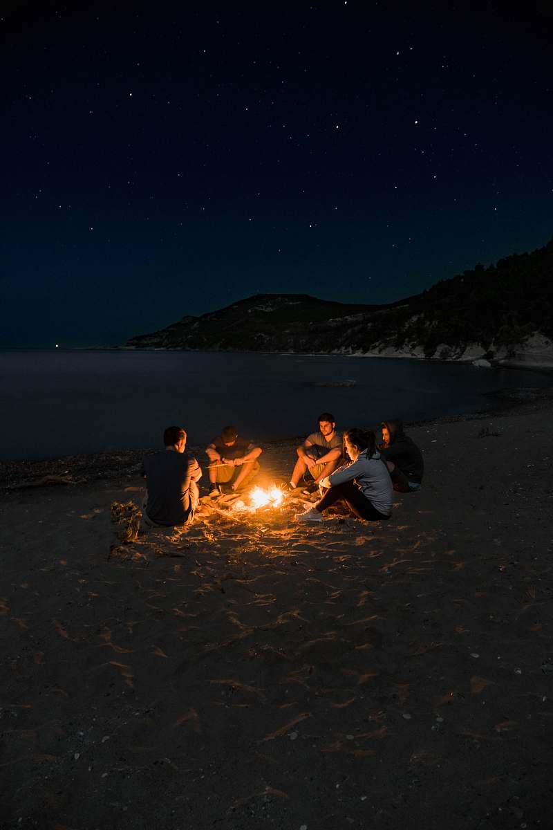 flame people sitting near campfire near seashore camping