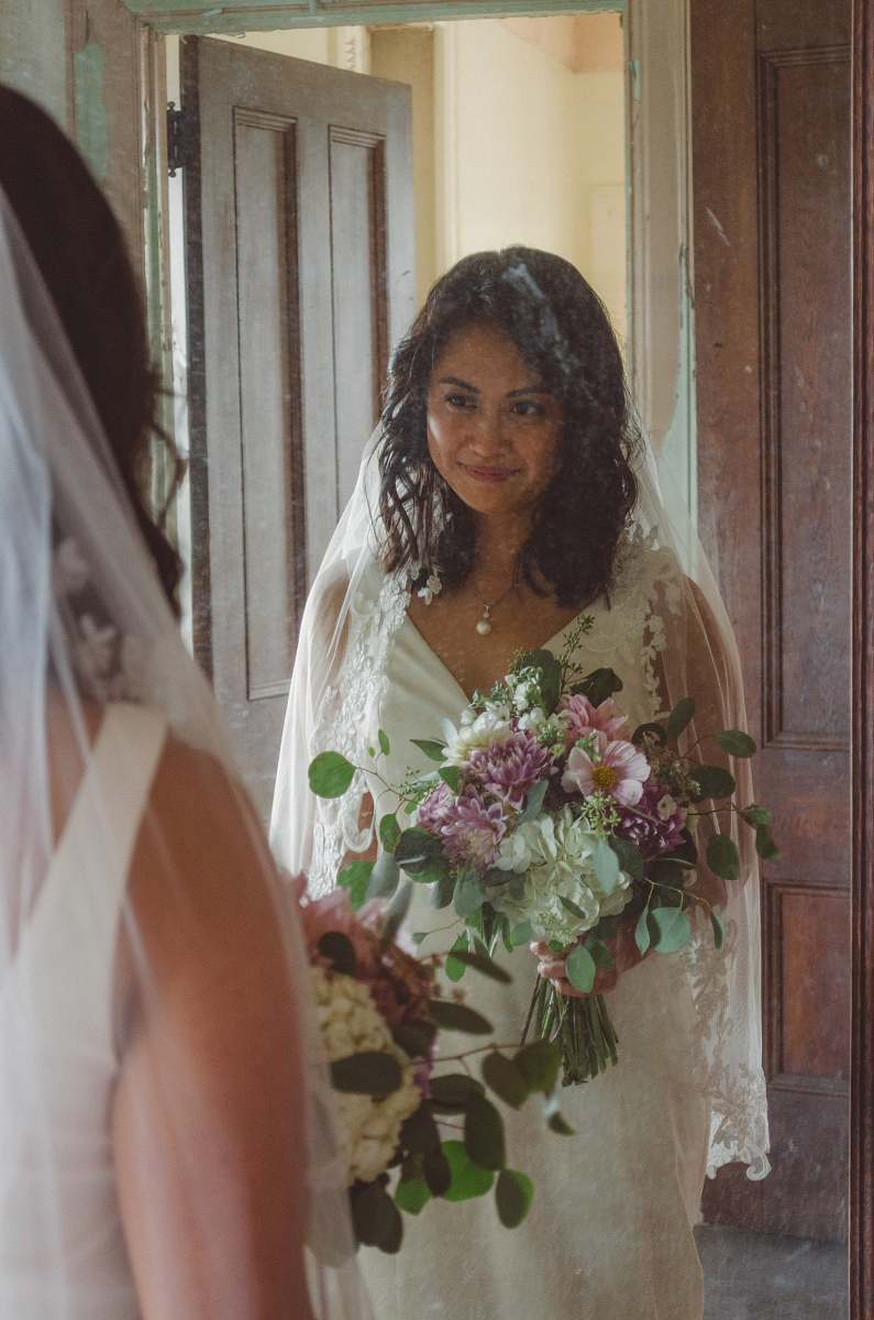 clothing smiling woman in front of mirror wearing white wedding gown and holding flowers human