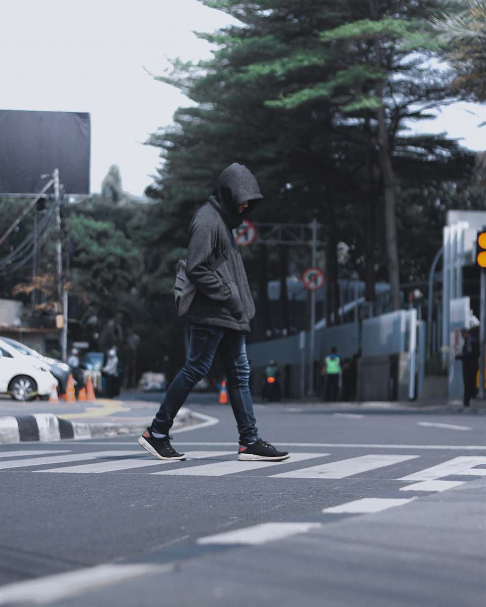 tarmac photography of man wearing black hooded jacket and blue denim jeans passing by the pedestrian lane road
