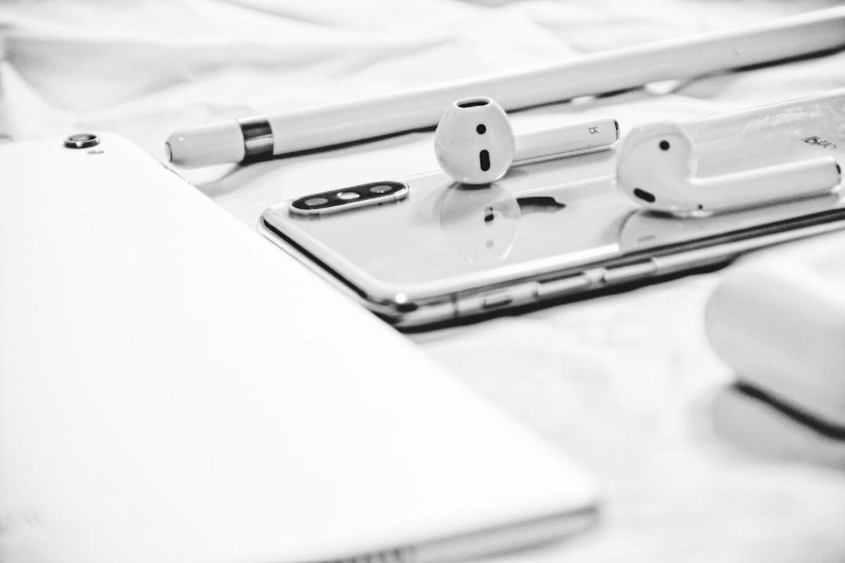 grey Apple AirPods on silver iPhone X beside Apple Pencil white