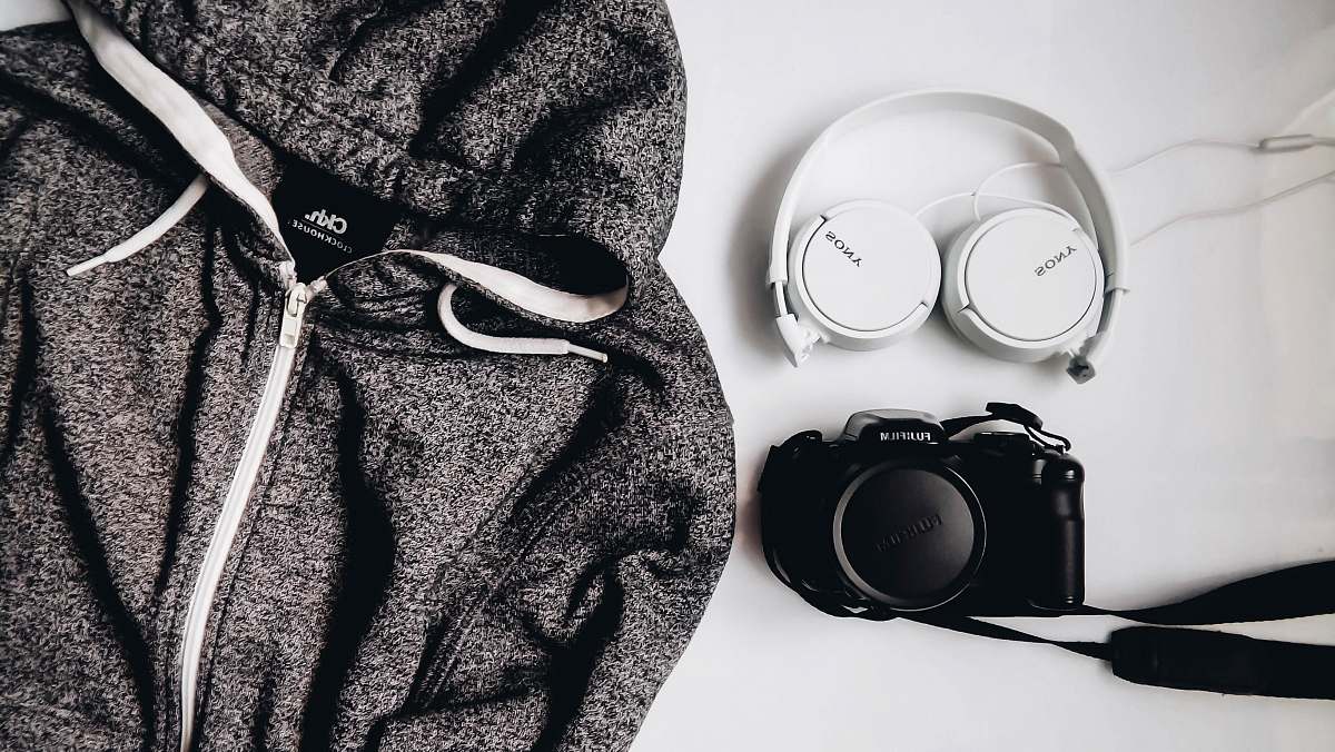 grey black DSLR camera and white Sony wireless headphones beside gray and white zip-up hooded jacket romania
