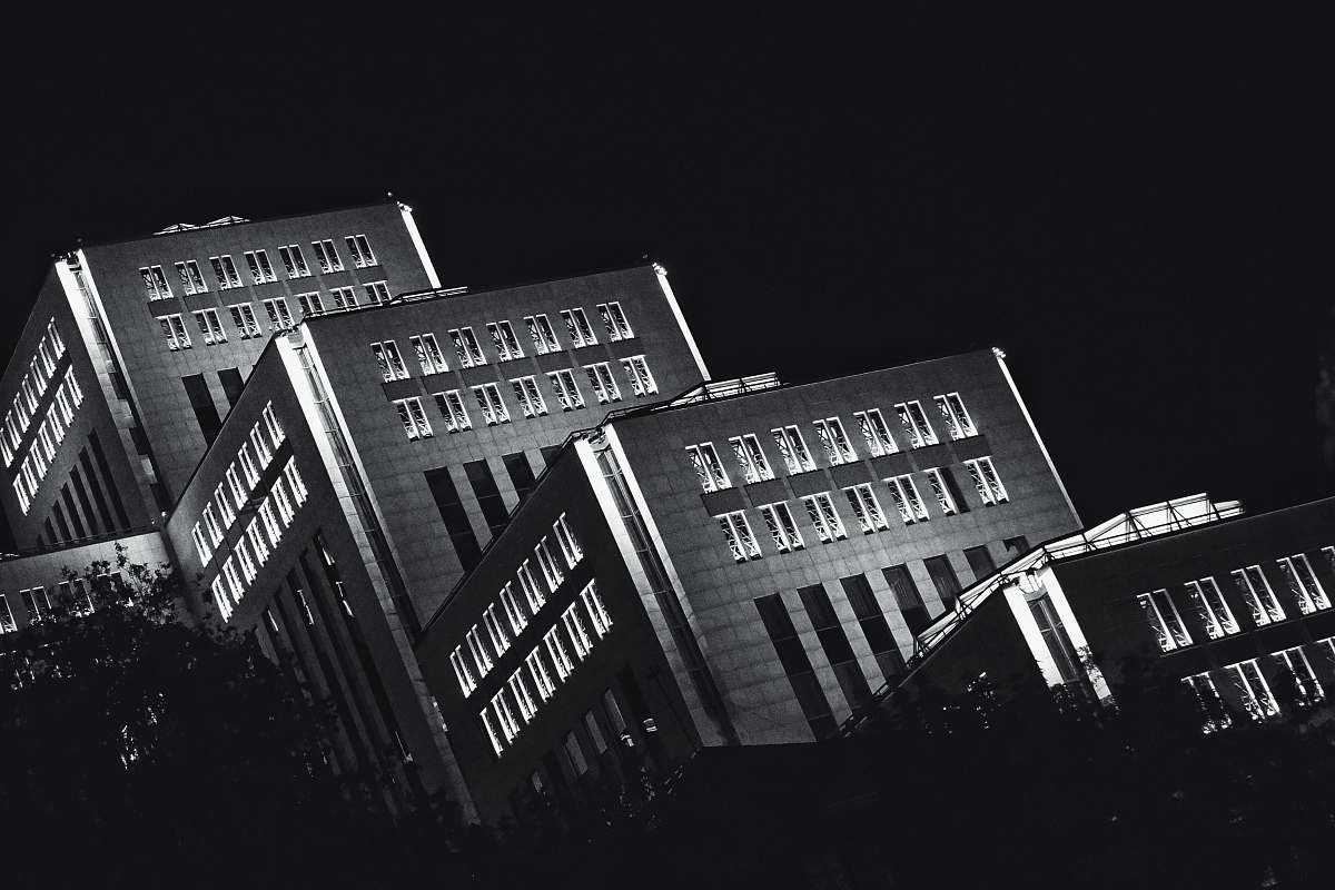 Experience the captivating allure of modern architecture with this striking black and white photograph featuring gray concrete office buildings illuminated against the night sky. The urban landscape, rendered in monochrome, highlights the intricate details and architectural elements of the buildings, making it a perfect addition for design projects, corporate presentations, or as a dramatic backdrop in editorial pieces. Ideal for showcasing the beauty of city life after dark.
