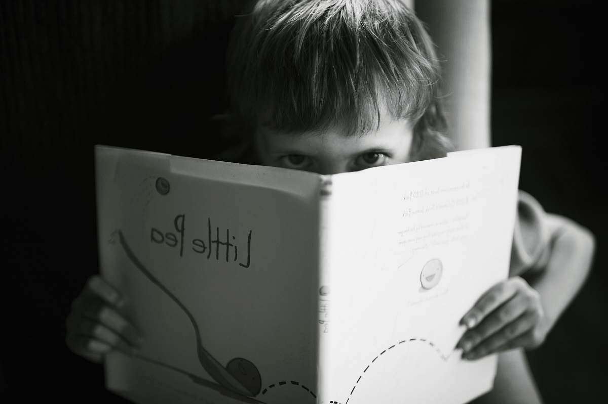 people grayscale photo of boy holding book reading