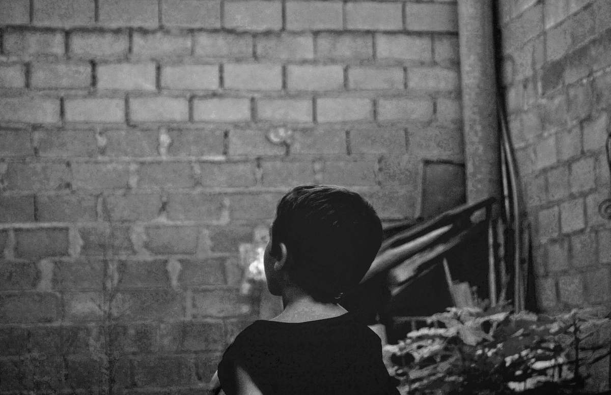brick grayscale photo of boy standing near wall xàtiva