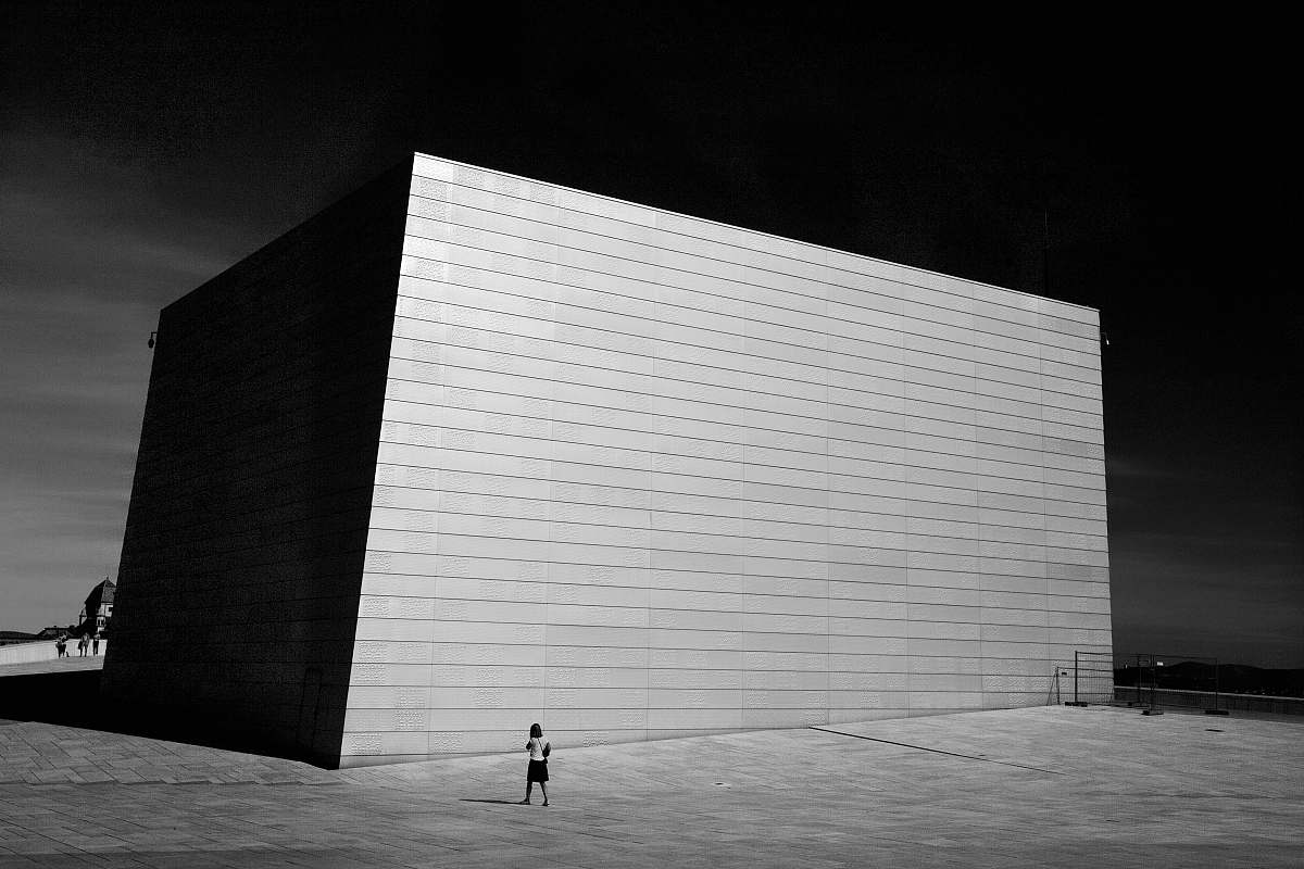 human grayscale photo of building and person walking beside person