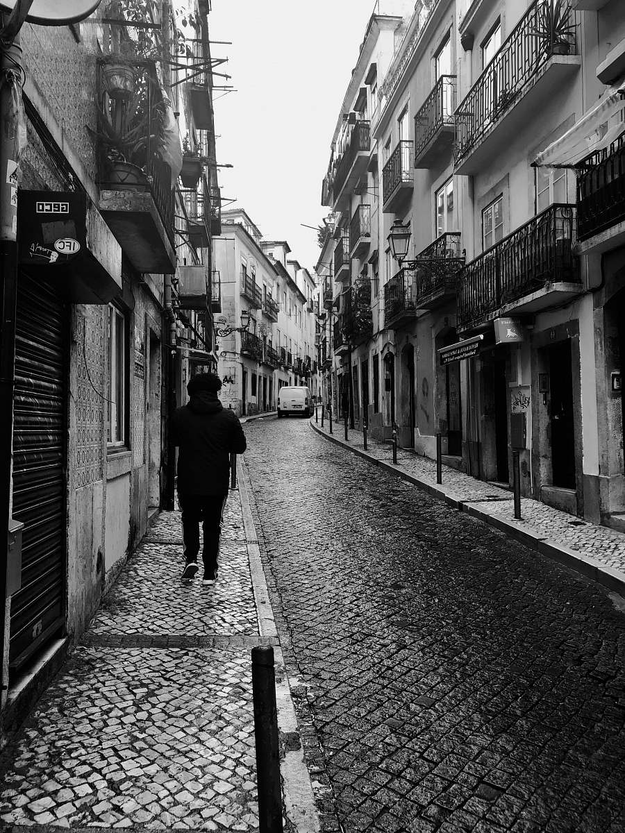 path grayscale photo of man on sidewalk between buildings walkway