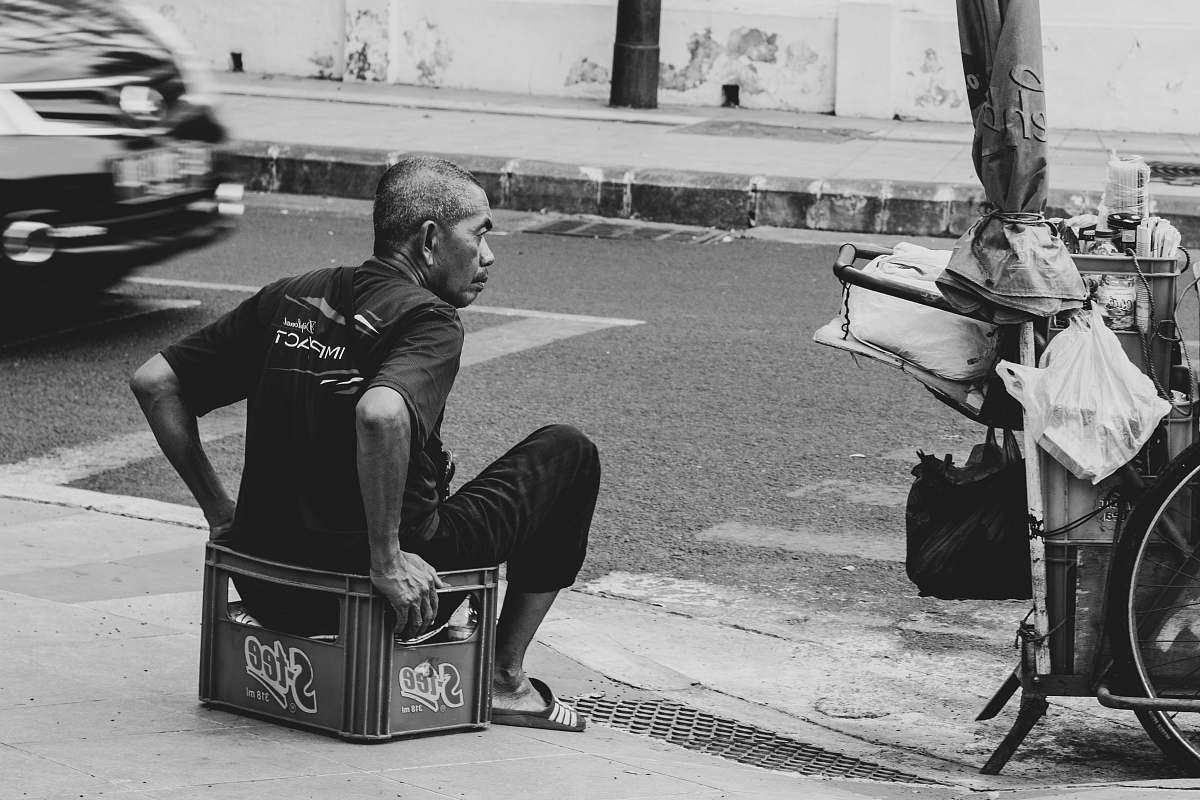 human grayscale photo of man sits on crate beside road person
