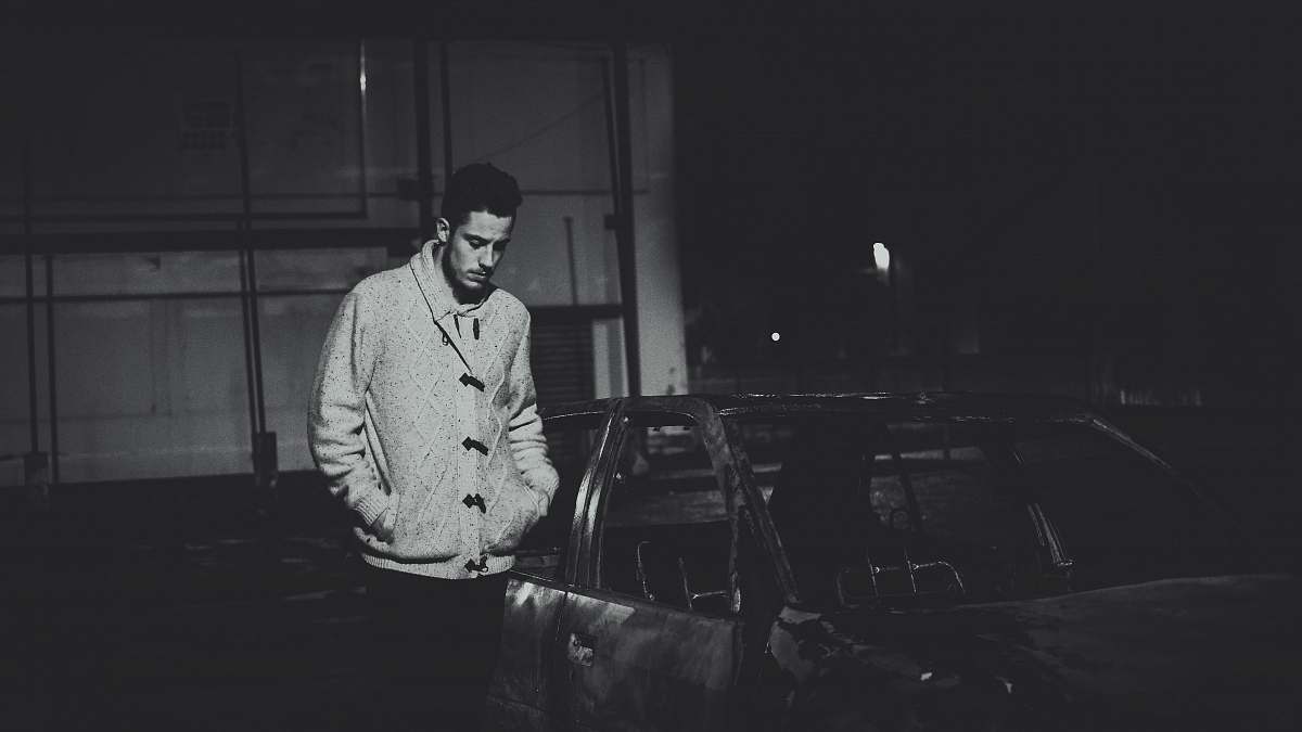 man grayscale photo of man standing beside car male