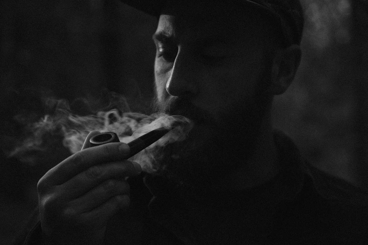 person grayscale photo of man using smoking pipe smoke