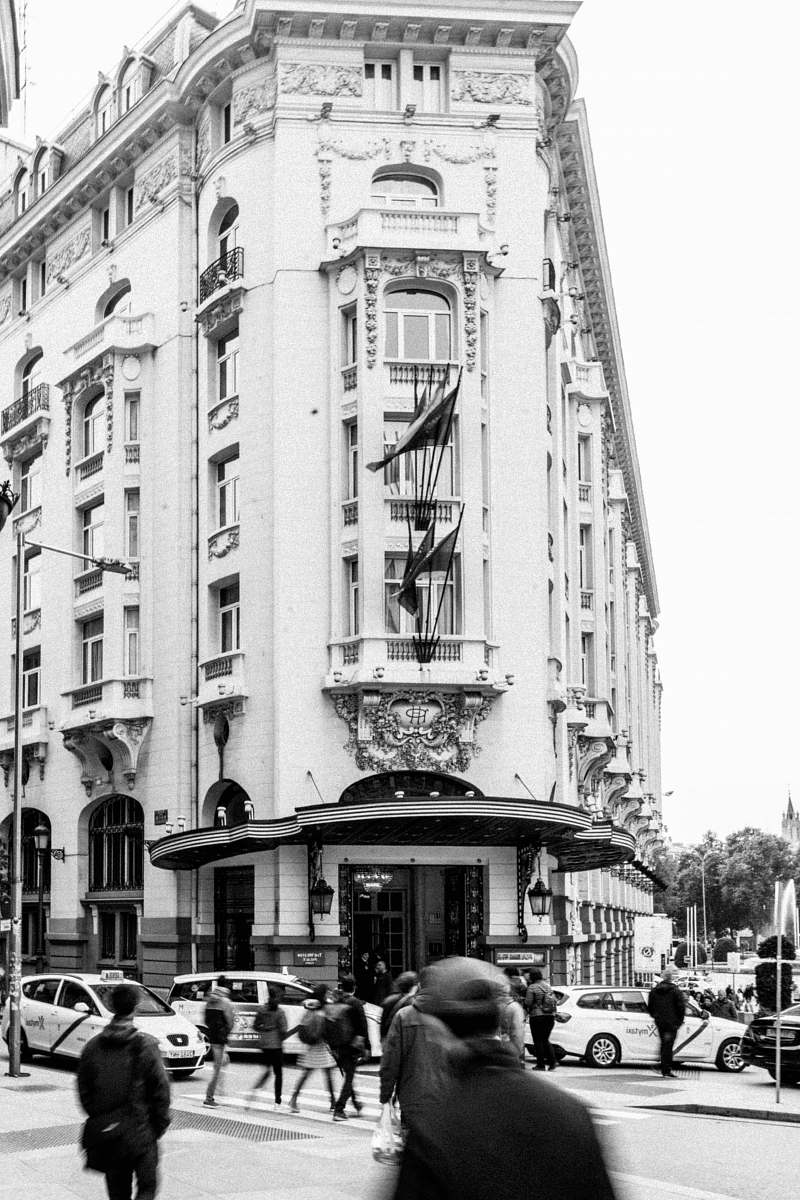 human grayscale photo of people and vehicles crossing street near building person