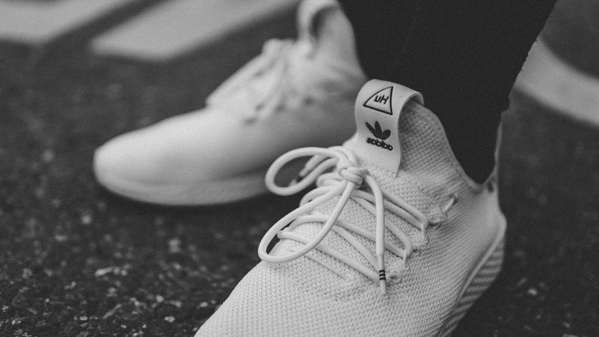 grey grayscale photo of person in white adidas low-top sneakers shoe