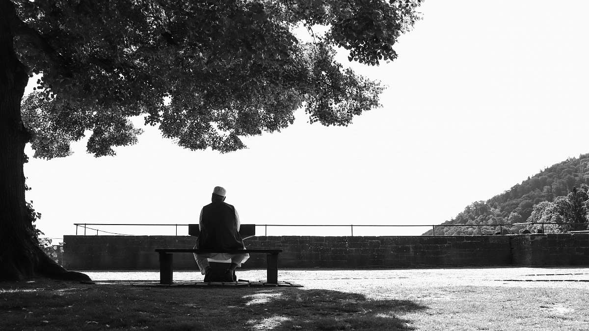 human grayscale photo of person sitting beside tree furniture