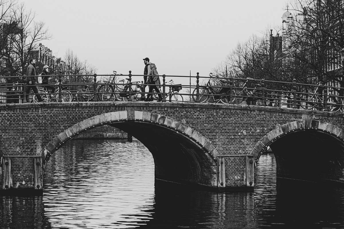 building grayscale photo of person walking on bridge water