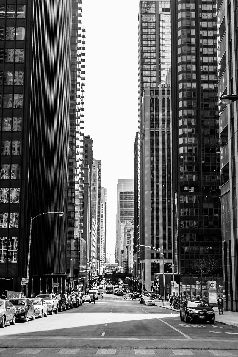city grayscale photo of road in between of tall buildings with vehicles urban