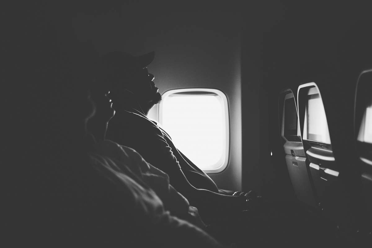 plane grayscale photo of three person sitting inside airplane window