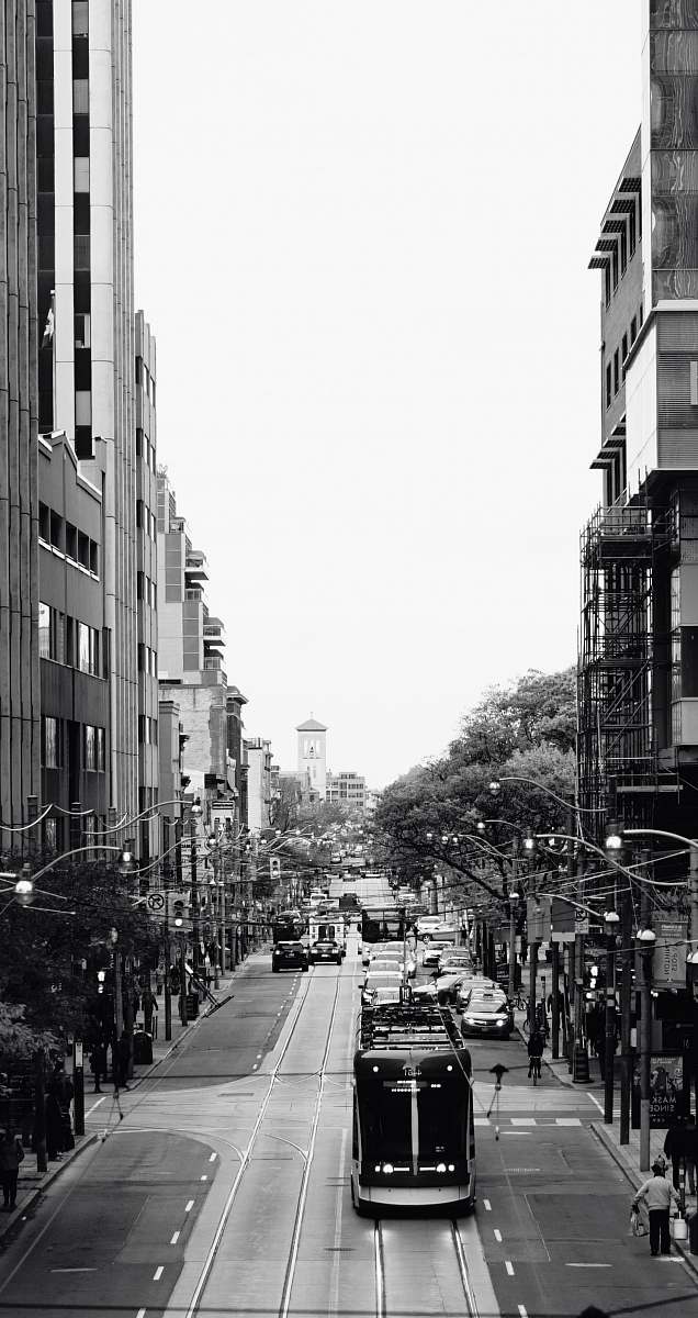 human grayscale photography of a tram passing by city street pedestrian