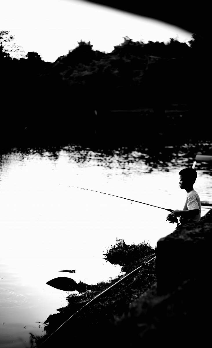 water grayscale photography of boy fishing on lake outdoors