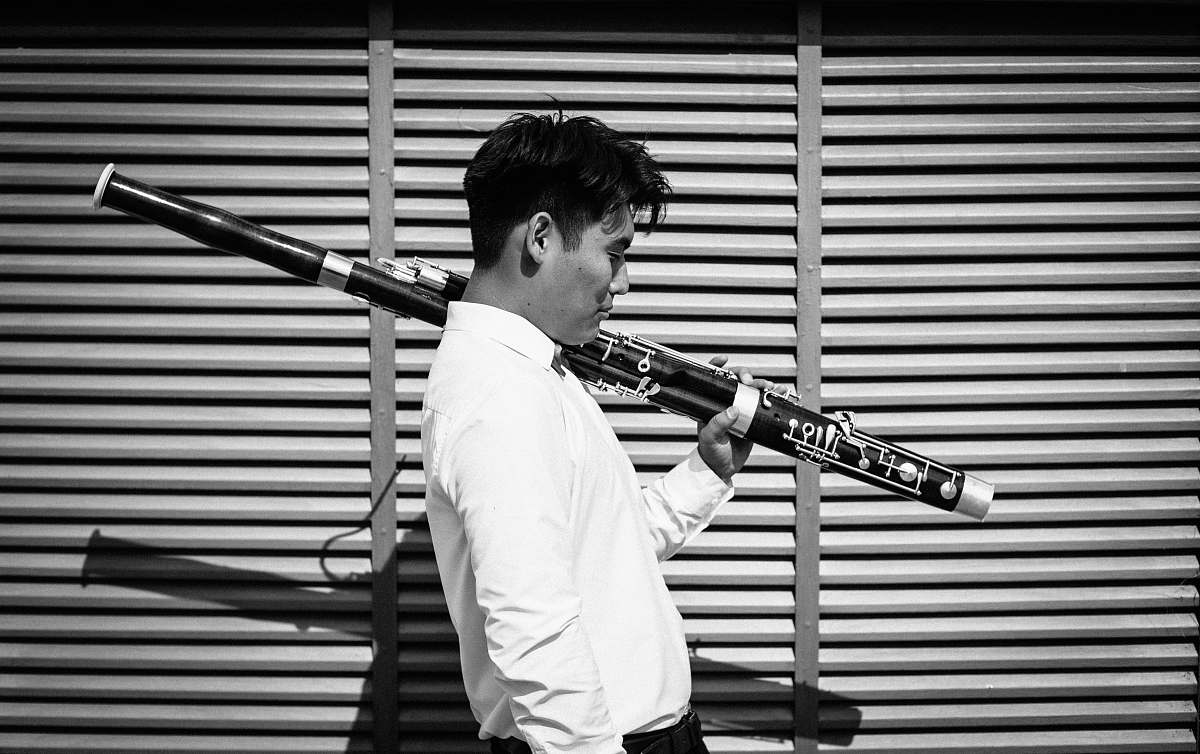 human grayscale photography of man carrying a wind instrument person
