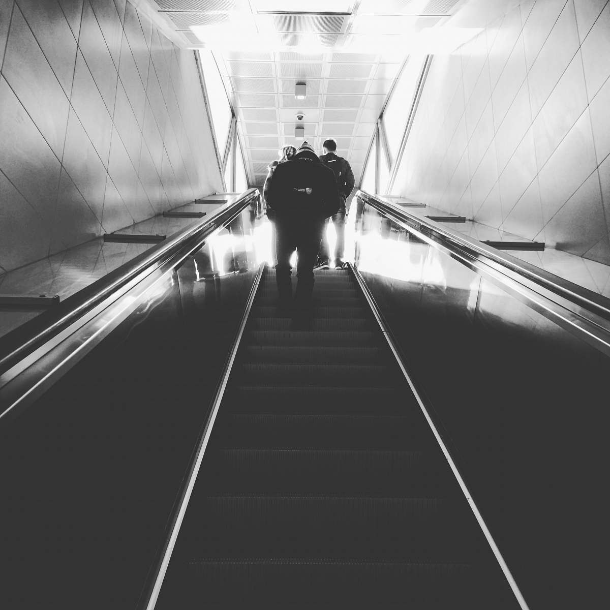 tunnel grayscale photography of man on escalator people