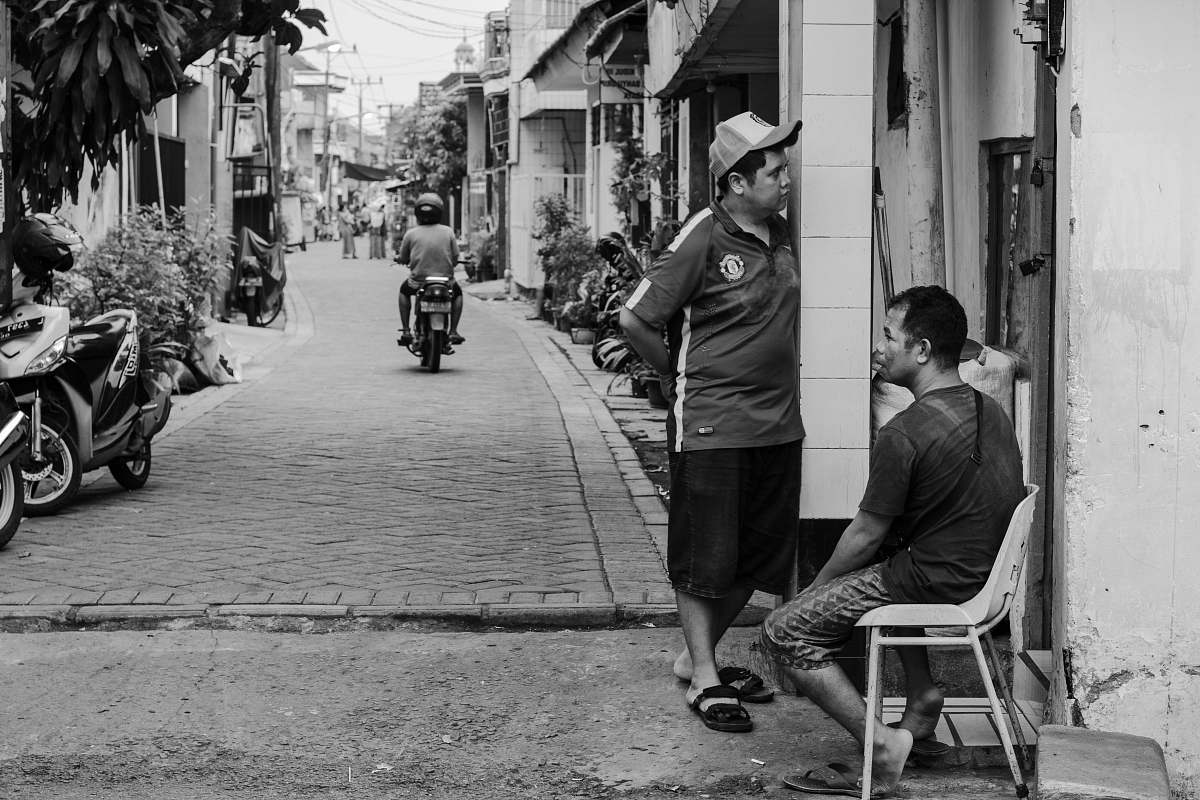 human grayscale photography of man sitting on chair beside standing man street