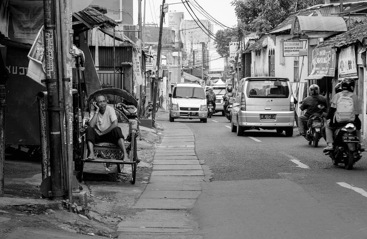 human grayscale photography of man sitting on chair near road street