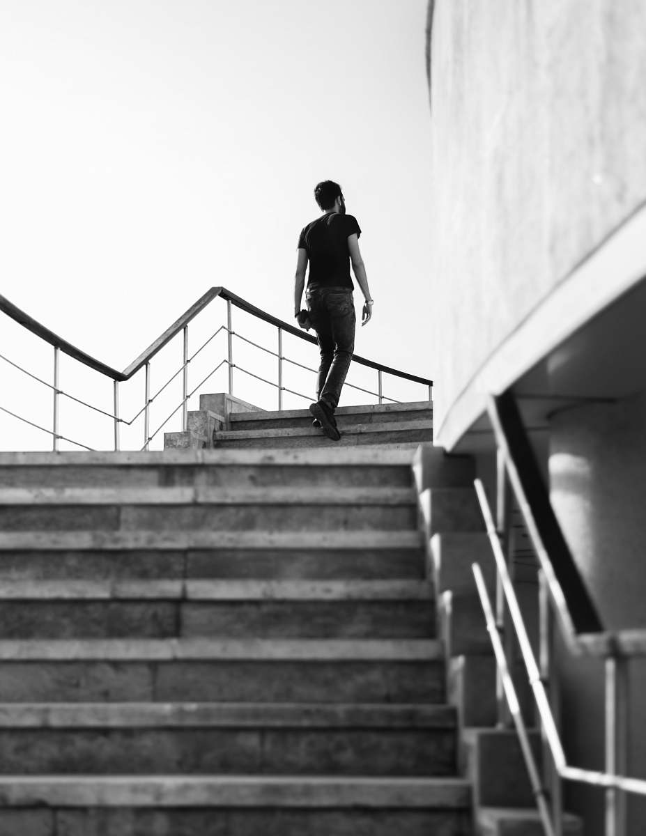 banister grayscale photography of man stepping on stairs handrail