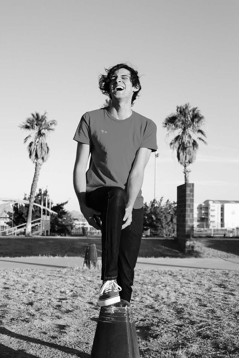 human grayscale photography of man wearing crew-neck t-shirt and pants standing and laughing in field person