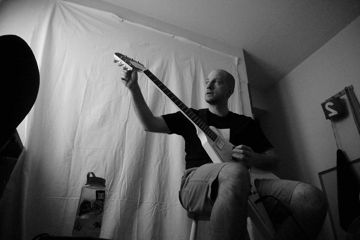 guitar grayscale photography of man wearing crew-neck t-shirt sitting while playing electric guitar human