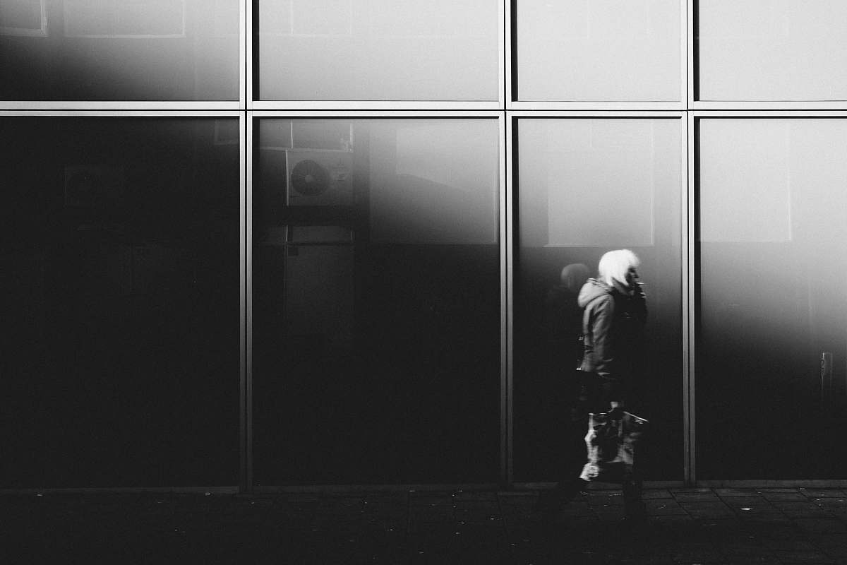 human grayscale photography of person walking near glass window building person