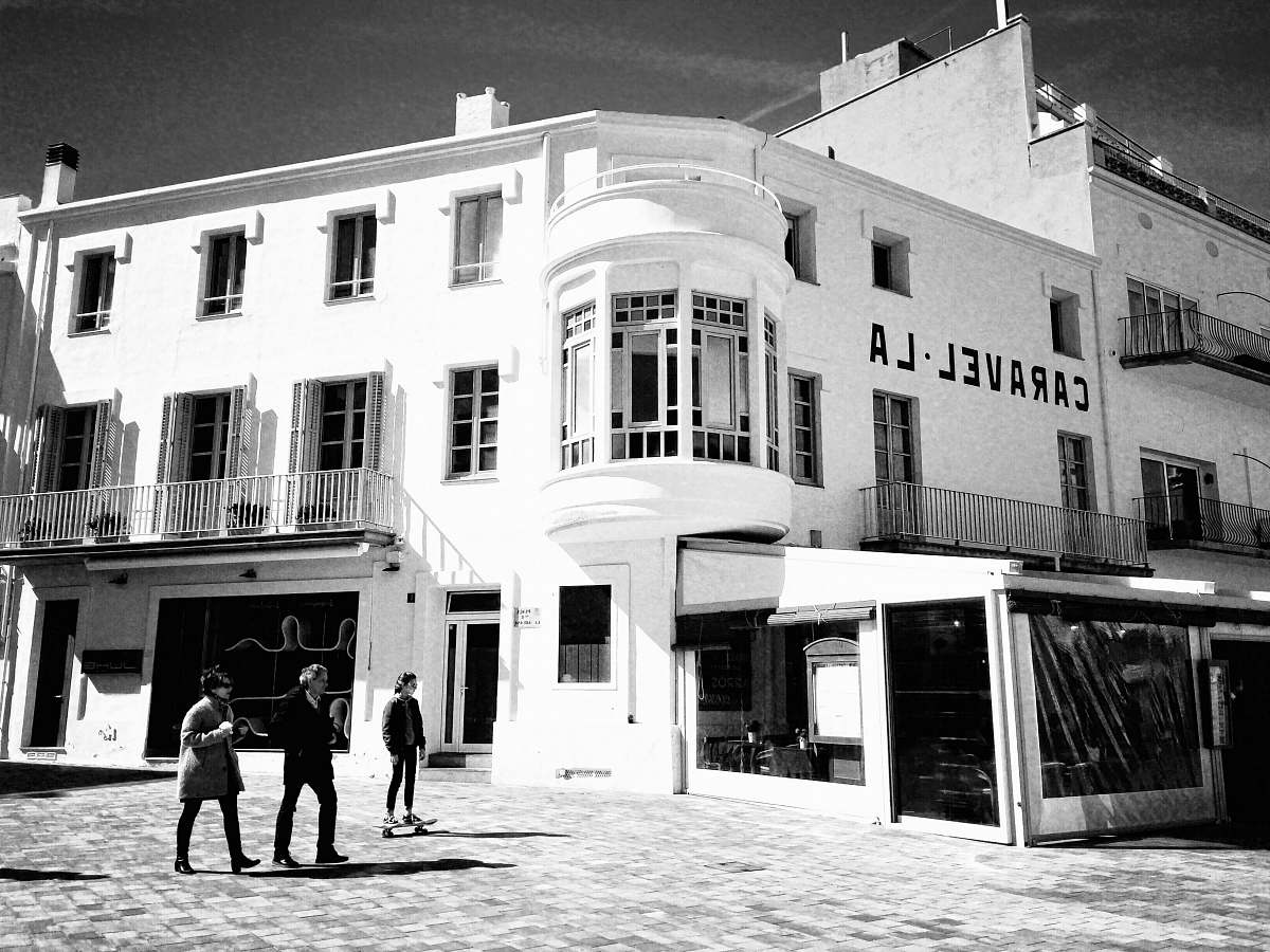 human grayscale photography of three person walking beside building person