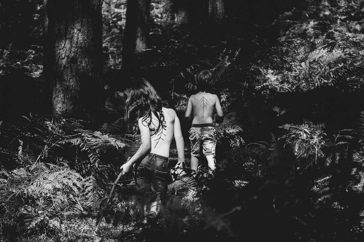 people grayscale photography of two topless persons standing at the forest during day human