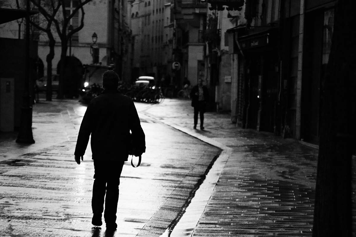 human grayscale photography of woman walking beside building pedestrian