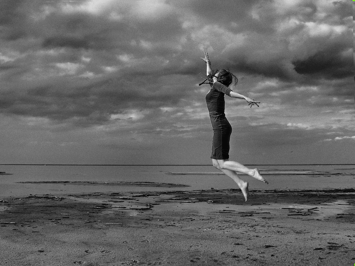 human graysclae photography of jumping woman near sea person