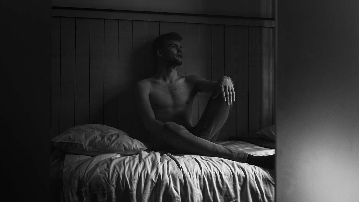 furniture greyscale photography of man sitting on bed bed