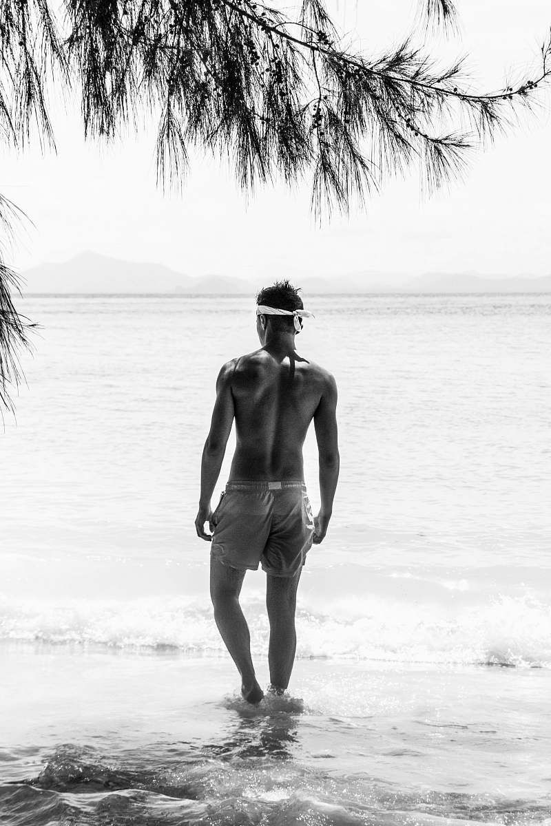 apparel half naked man in shorts with white bandana standing on shore during daytime back