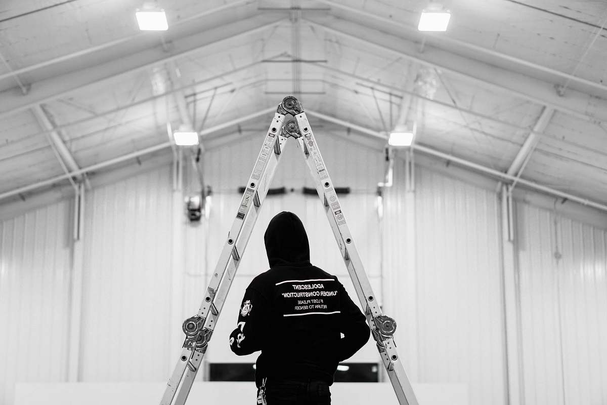 human low saturation photography of person in black hooding standing infront of ladder person