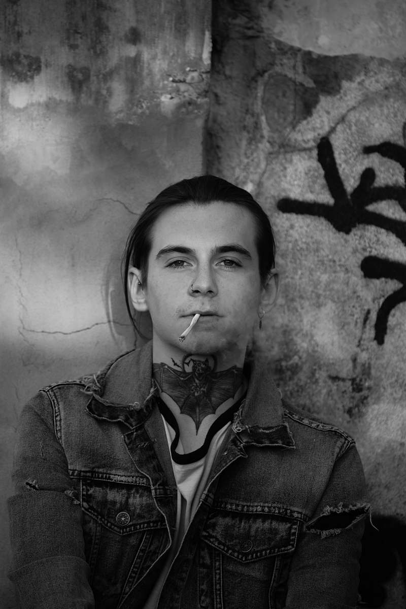 human man in denim jacket leaning on wall with cigarette on mouth smoking