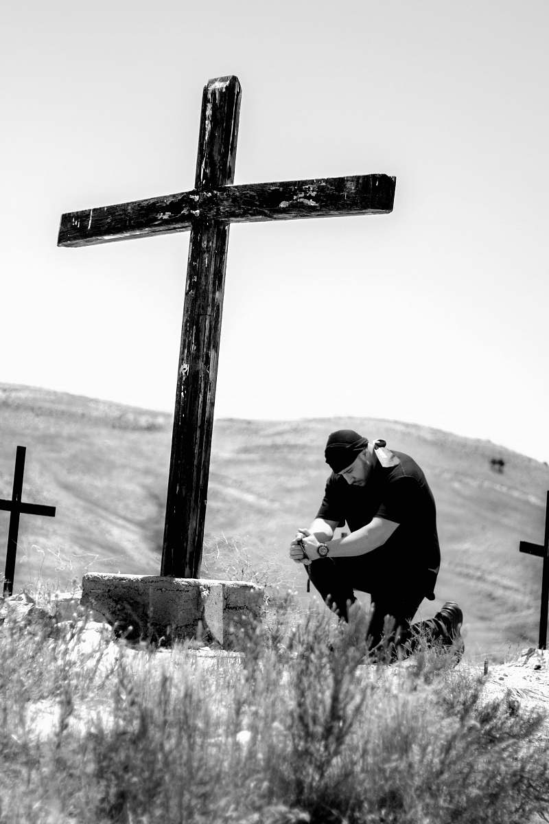 symbol man kneeling in front of wooden cross cross