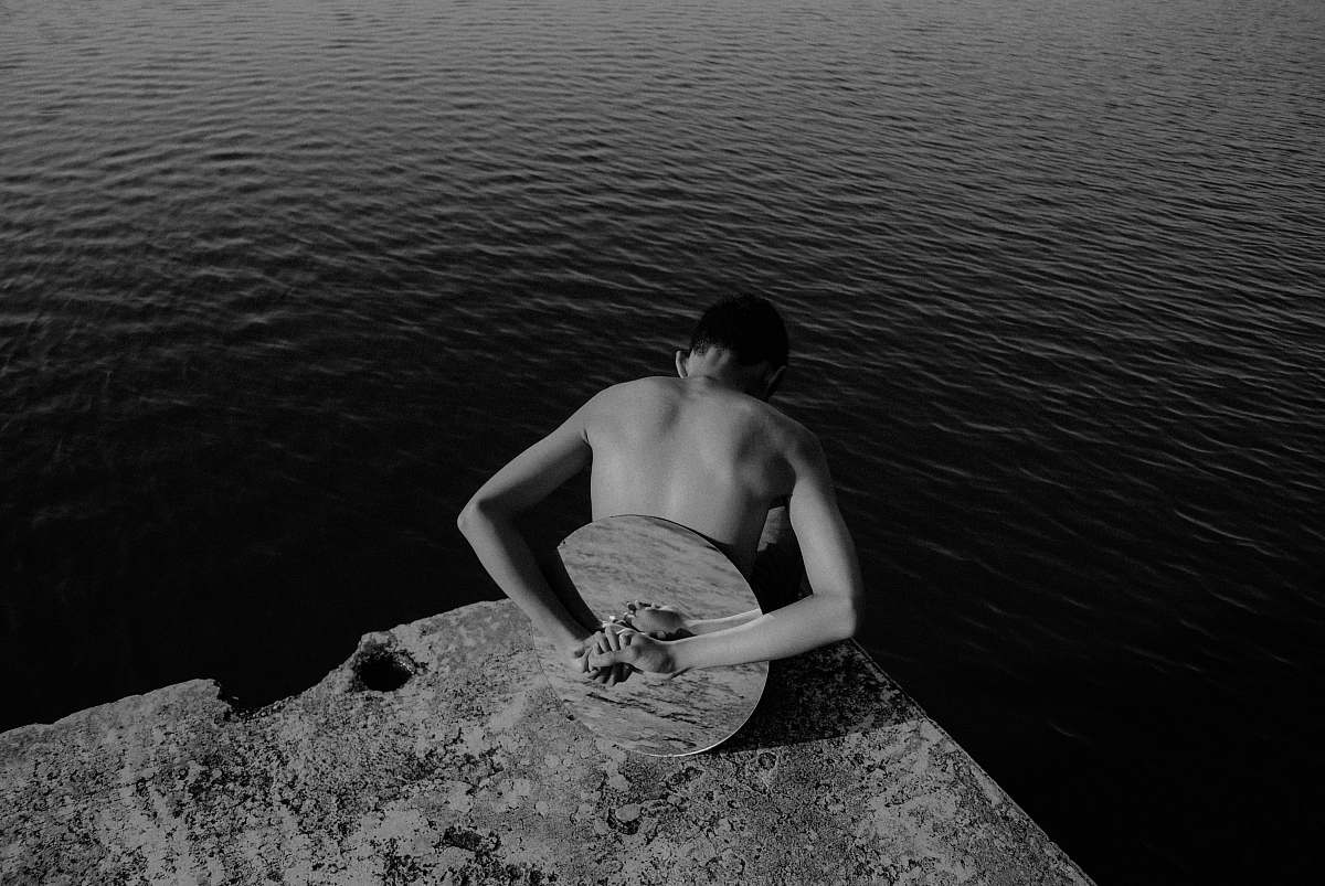 back man with round mirror on his back at the edge of rock island facing body of water danau buatan