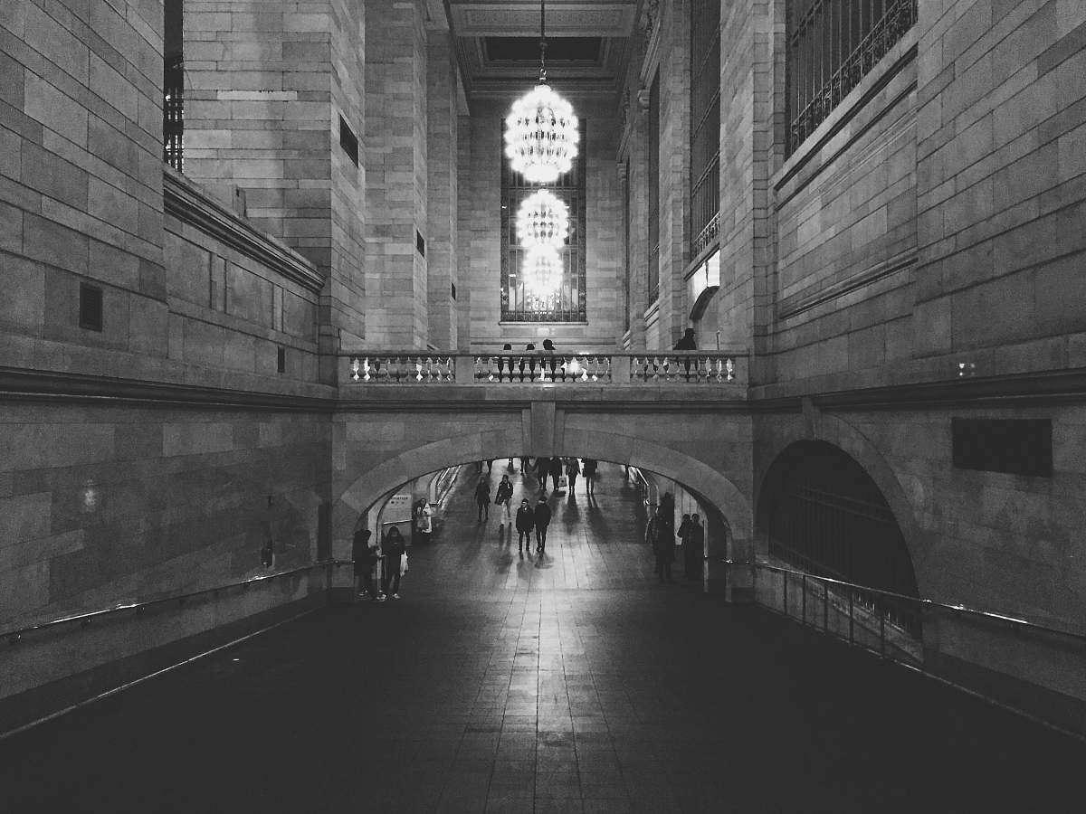 architecture people walking on hallway of concrete building with turned on chandelier lights in grayscale photography new york