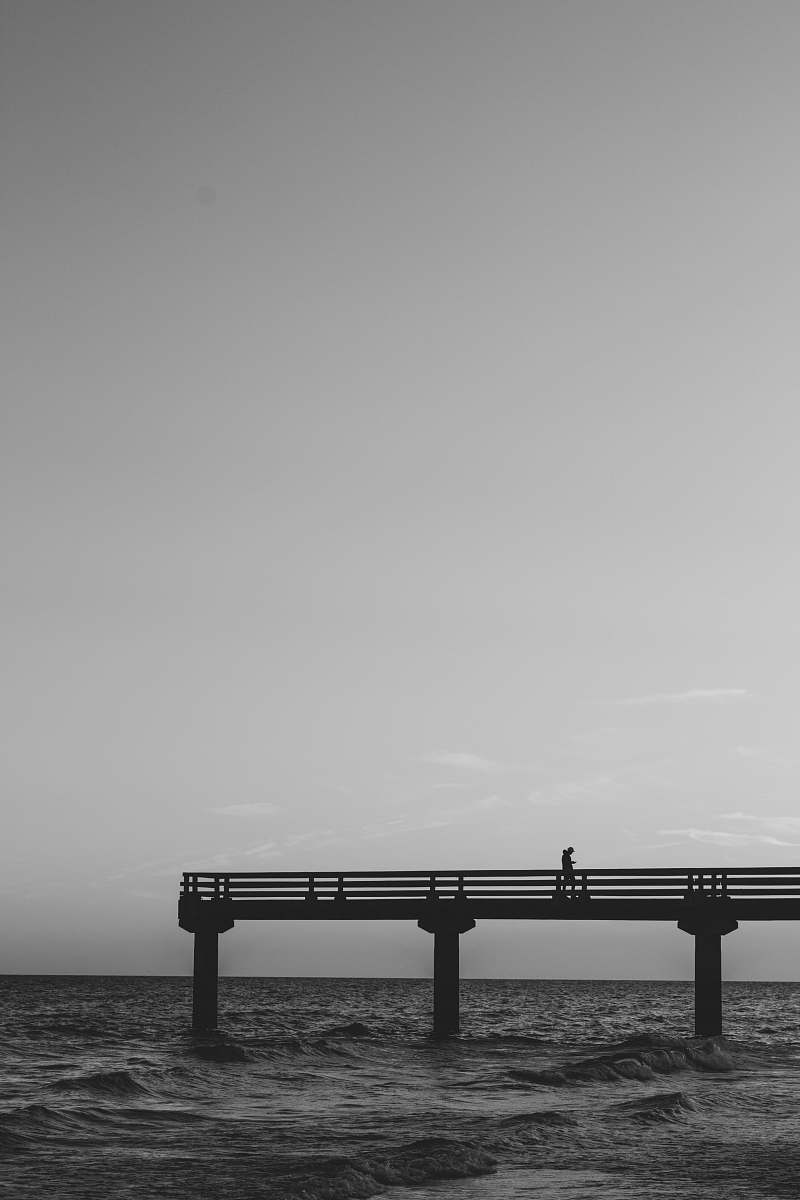 grey person standing near beach dock water