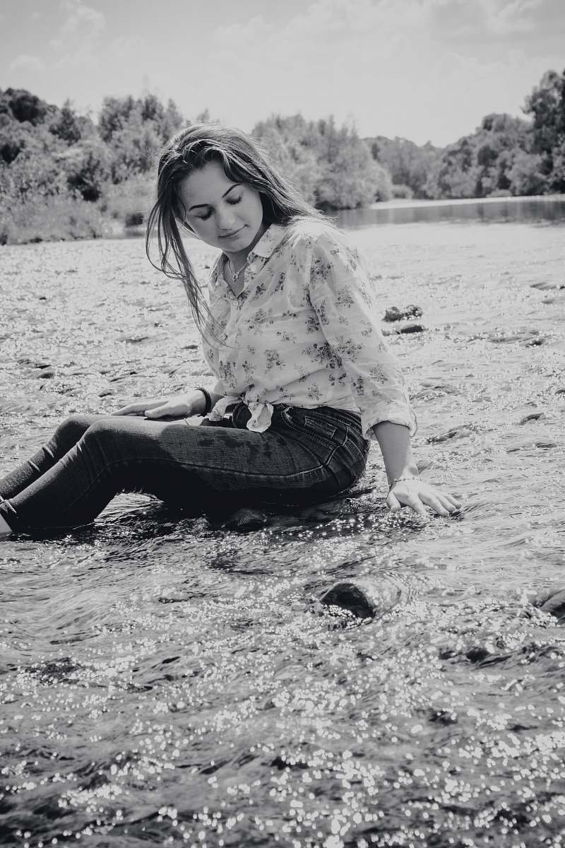 human smiling woman sitting on rocks surrounded by water person