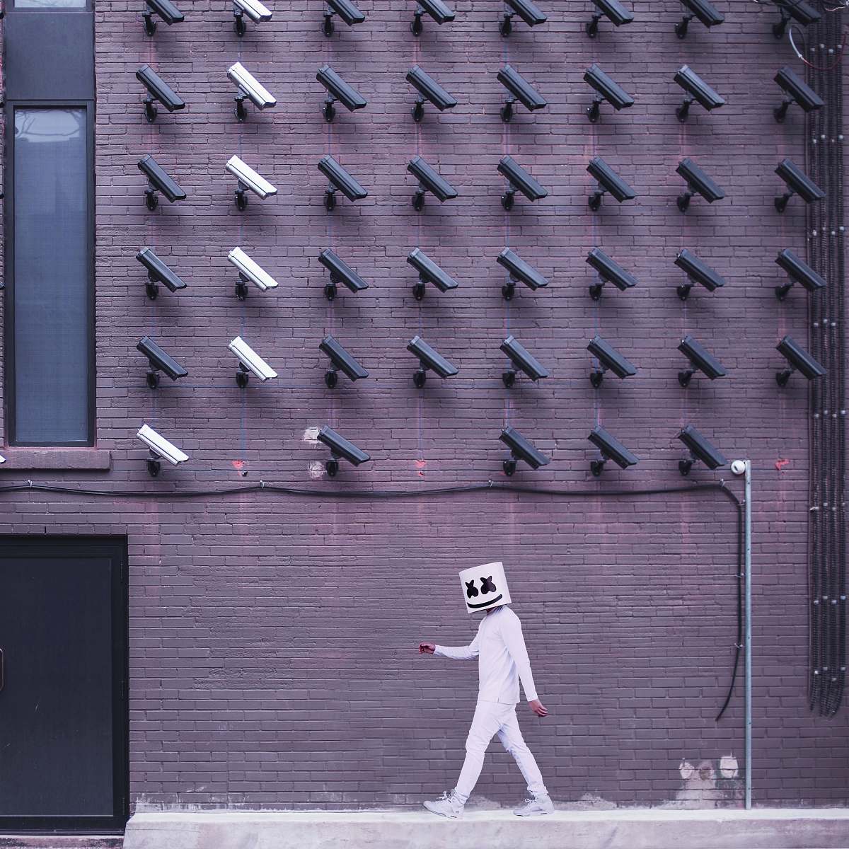 grey Marshmello walking down the side of the road with camera on the top of the building costume