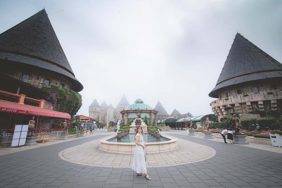 city woman wearing white dress standing in front of water fountain downtown