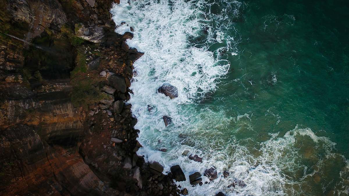 waves aerial photography of brown cliff near body of water rock