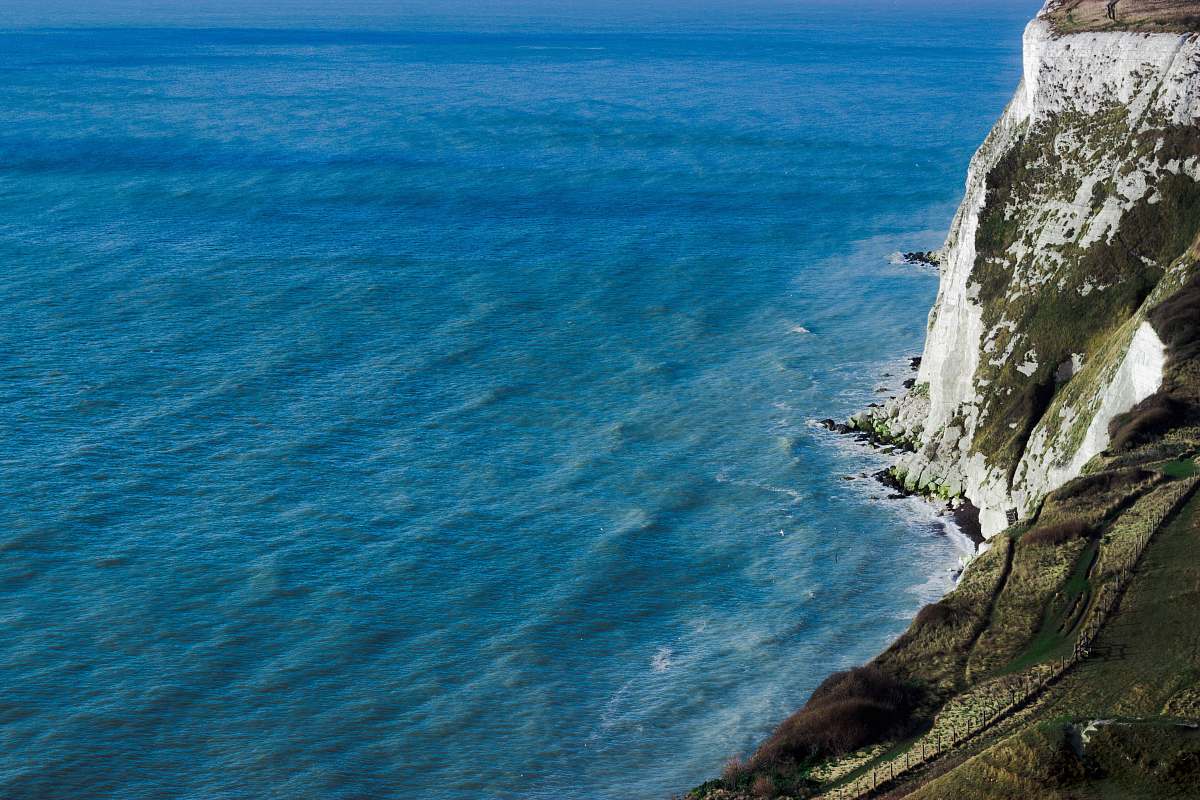 coast aerial photography of mountain cliff beside seashore during daytime ocean